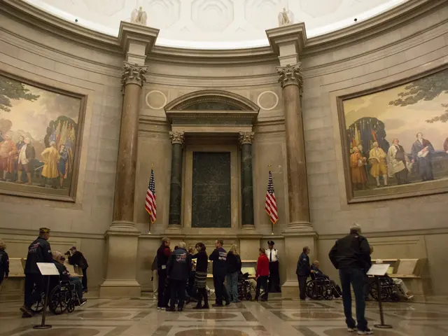 The image shows a group of people standing in front of a building with a rotunda. There are people...