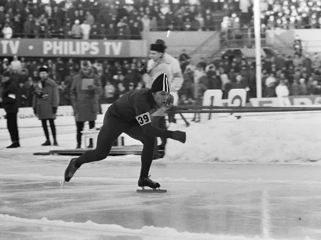 The image shows a man speed skating on an ice rink in front of a crowd. He is wearing a black and...