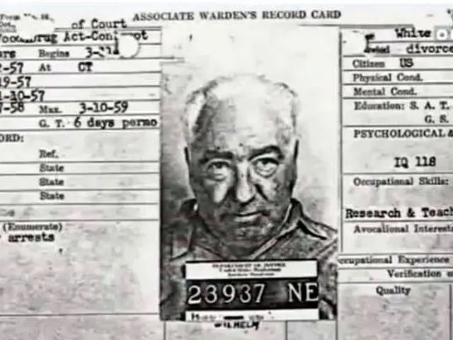 The image shows a black and white mug shot of a man with a number plate, which is believed to be...