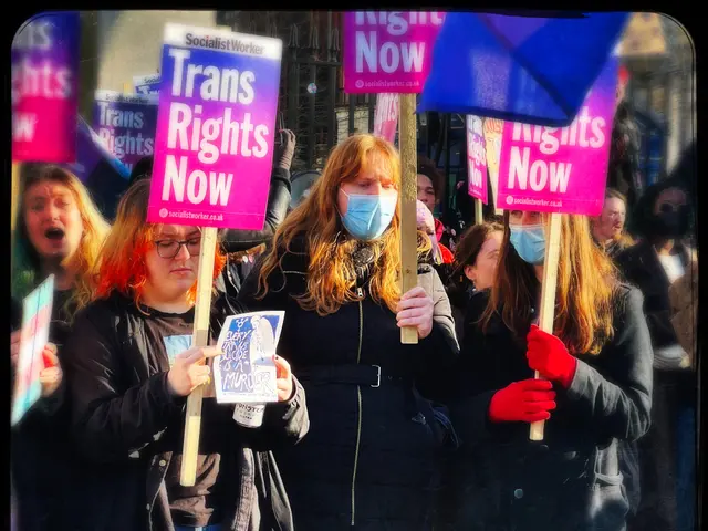 The image shows a group of people standing on the road, some of them wearing masks and holding...