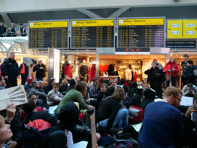 The image shows a large group of people sitting in an airport, some of them holding bags and...