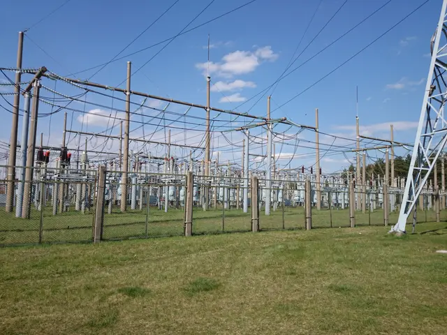 The image shows an electrical substation in the middle of a grassy field, surrounded by a fence and...