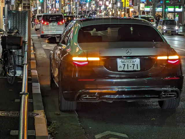 The image shows a Mercedes-Benz S-Class driving down a city street at night. On the left side of...