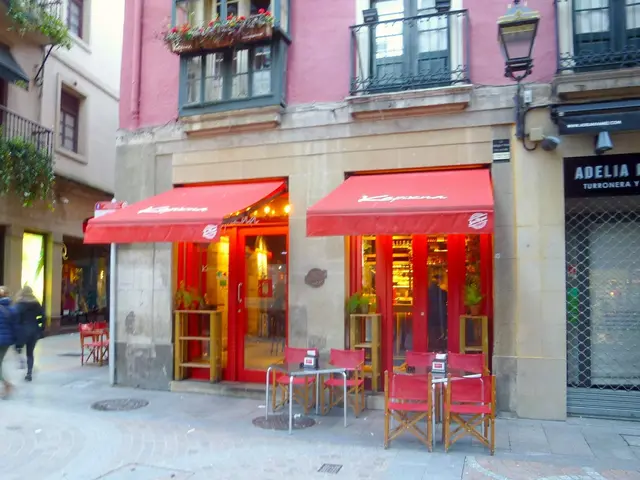 The image shows a restaurant with red awnings on the side of a street, surrounded by buildings with...