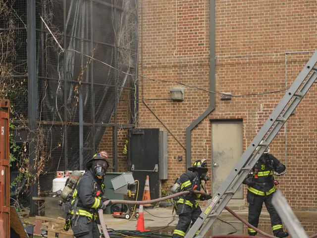 The image shows a group of firefighters wearing helmets and holding pipes in their hands, working...