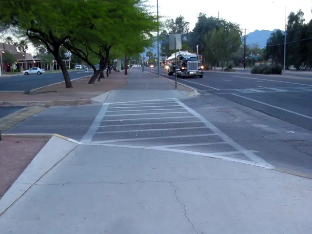 The image shows a city street with vehicles driving on it, a sidewalk with a caution sign on it...