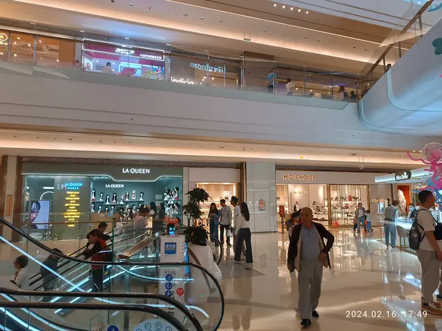 The image shows the inside of a shopping mall with people walking around, some of them carrying...