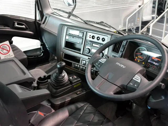 The image shows the interior of a truck with a steering wheel, dashboard, seats, gear rod,...