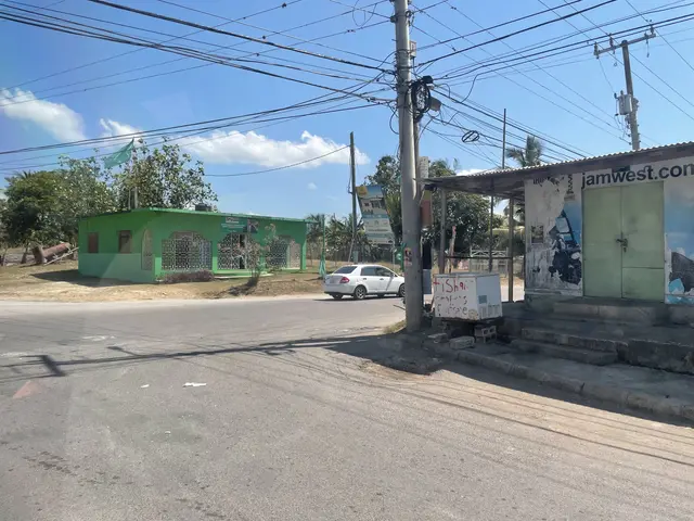 The image shows a street with a car parked on the side of it, electric poles with wires, a shed...