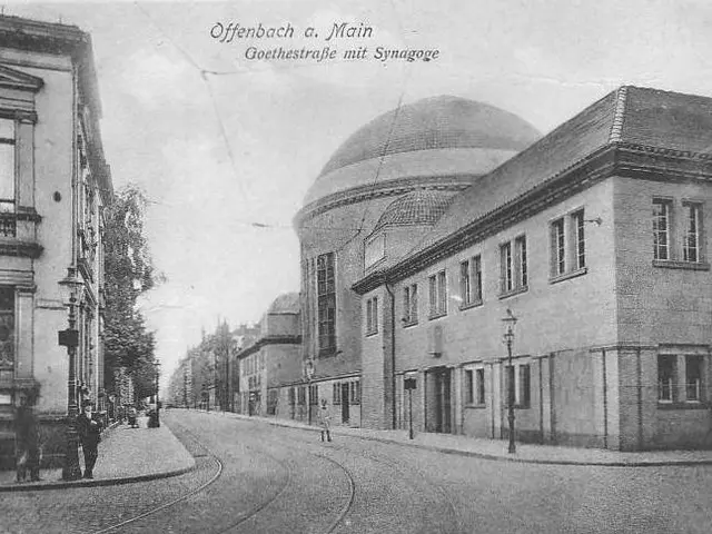 The image shows an old black and white photo of a city street with buildings, street poles, street...