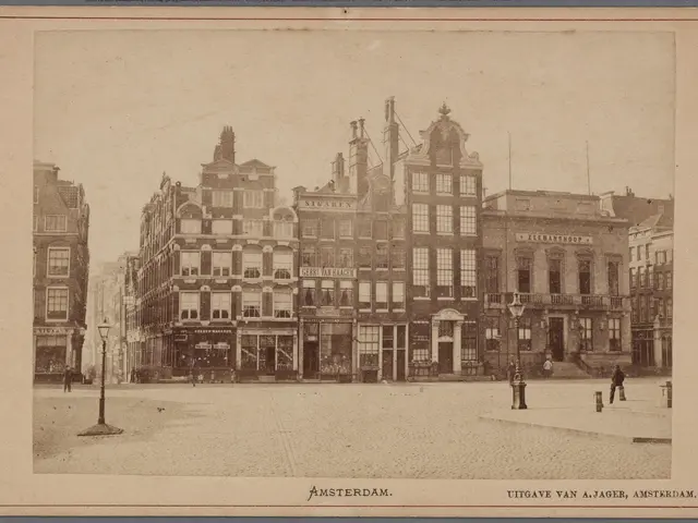 The image shows an old black and white photo of a city street with buildings, street poles, street...