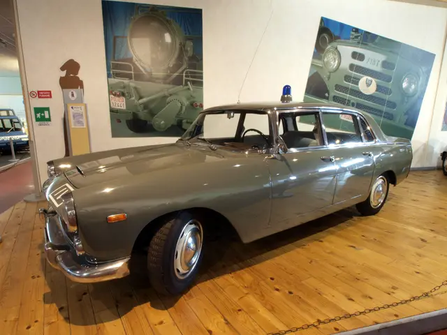 The image shows an old car on display in a museum, surrounded by a chain, poles, boards, and other...