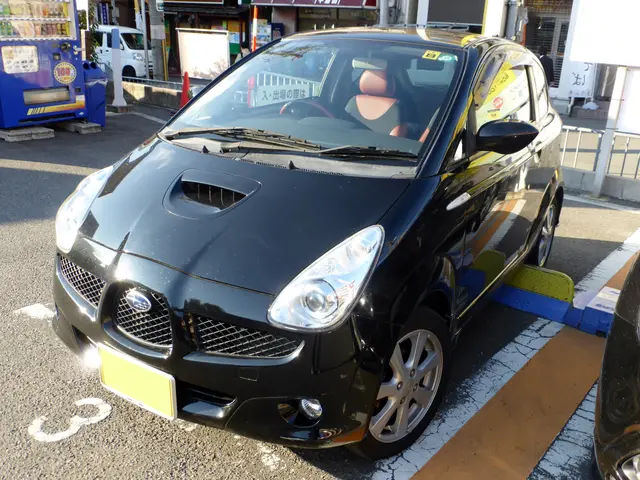 The image shows a black car parked in a parking lot next to a vending machine on the left side of...