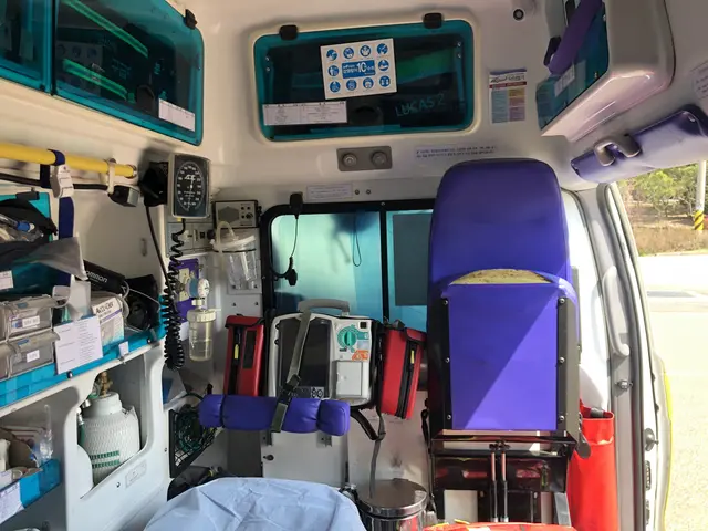 The image shows the inside of an ambulance with a blue chair, a table, a dustbin, and various...
