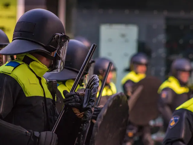 The image shows a group of police officers in riot gear standing next to each other, wearing...