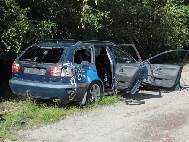 The image shows a blue car that has been involved in a crash on the side of the road, surrounded by...