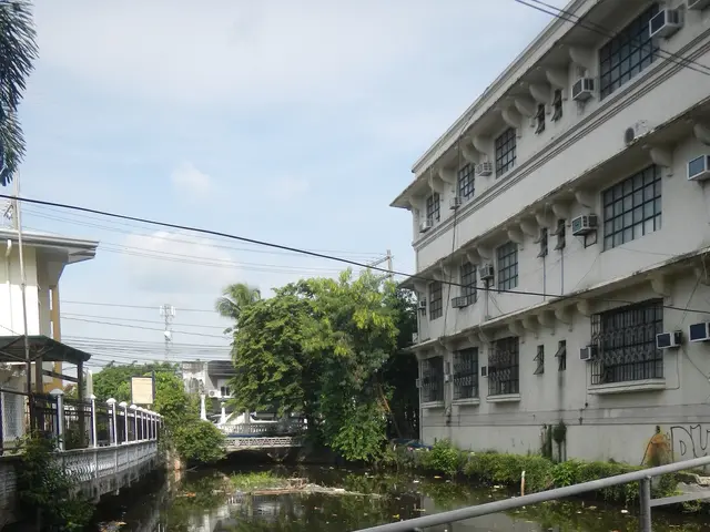 The image shows a small canal running through a city street next to tall buildings, with a railing...