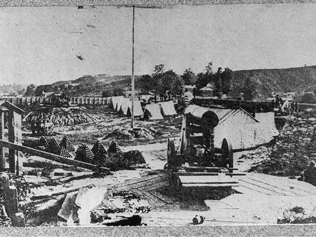 The image shows a black and white photo of a construction site with a machine in the foreground,...