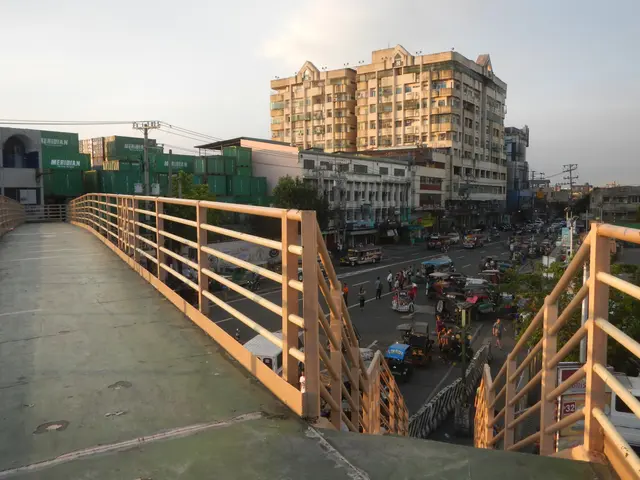 The image shows a pedestrian bridge with railings spanning a busy street filled with lots of...
