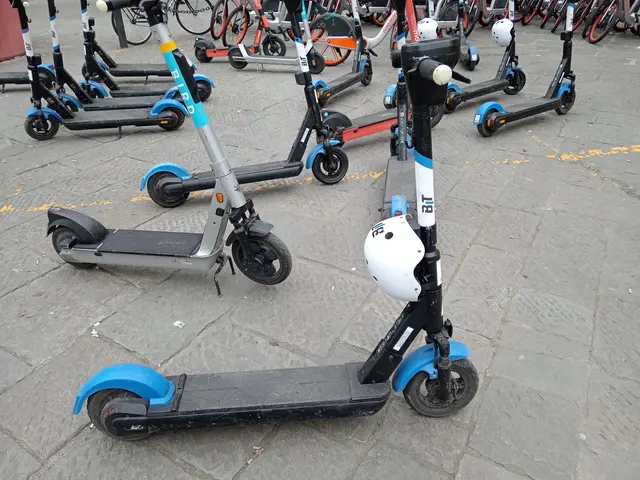 The image shows a row of electric scooters parked on the side of a street, with bicycles, poles,...