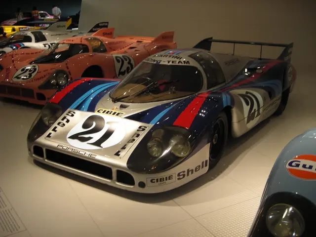 The image shows a Porsche 917K Le Mans race car on display in a museum, surrounded by other sports...
