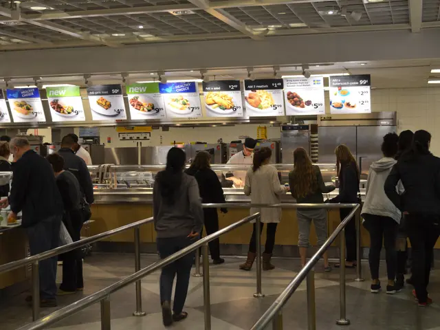 The image shows a group of people standing in line at a fast food restaurant. There are railings in...