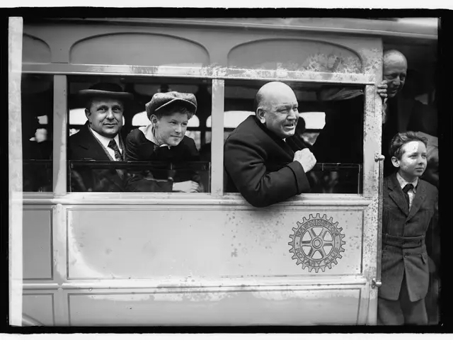 The image shows a black and white photo of a group of people riding on top of a bus. There are...