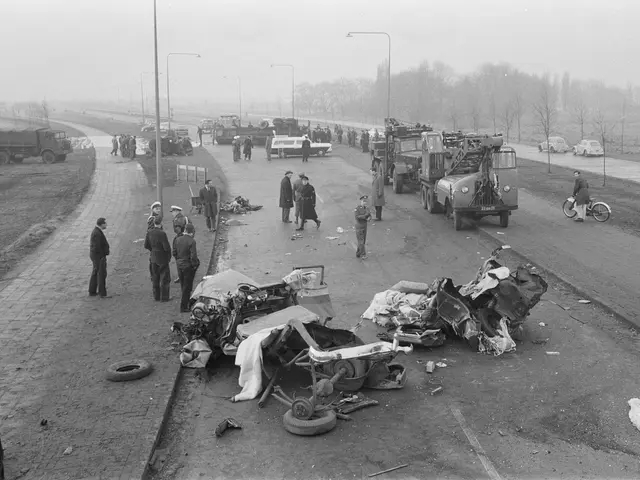 The image shows a black and white scene of a car accident on the side of a road. There are many...