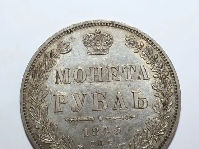 The image shows a silver coin with a crown on it against a white background. The text on the coin...