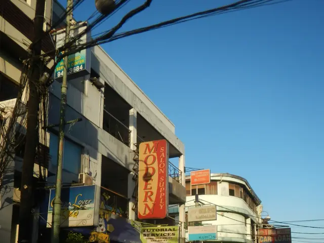 The image shows a city street filled with lots of tall buildings, electric poles, electric cables,...