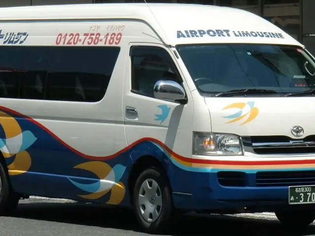 The image shows a white and blue van parked on the side of the road, with a building in the...