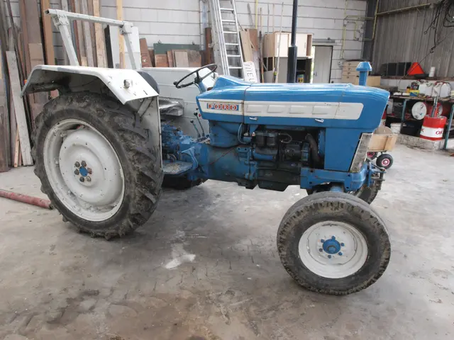 The image shows a blue tractor parked in a garage next to a building. The tractor is on the ground...