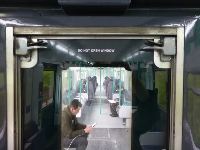 The image shows a man sitting on a train, looking at his cell phone. He is surrounded by other...