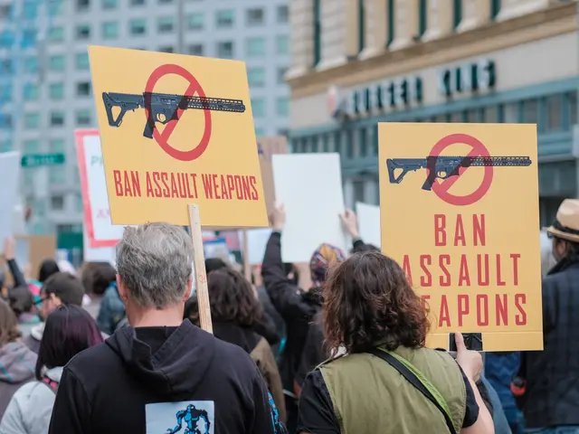 The image shows a group of people walking down a street, holding signs that read "Ban Assault...