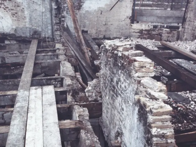 The image shows an old building with a lot of rubble on the ground, consisting of wooden planks and...