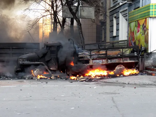 The image shows a truck engulfed in flames on the side of a street, with smoke billowing out of it....