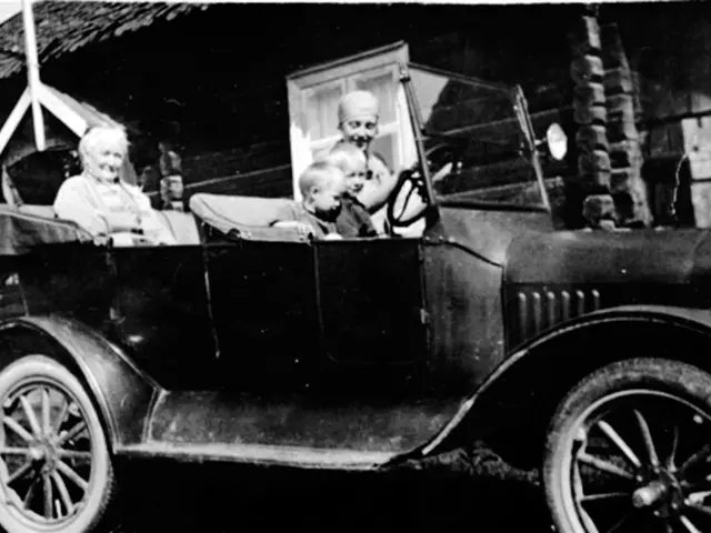 The image shows an old black and white photo of a family in an old car, with two adults and two...