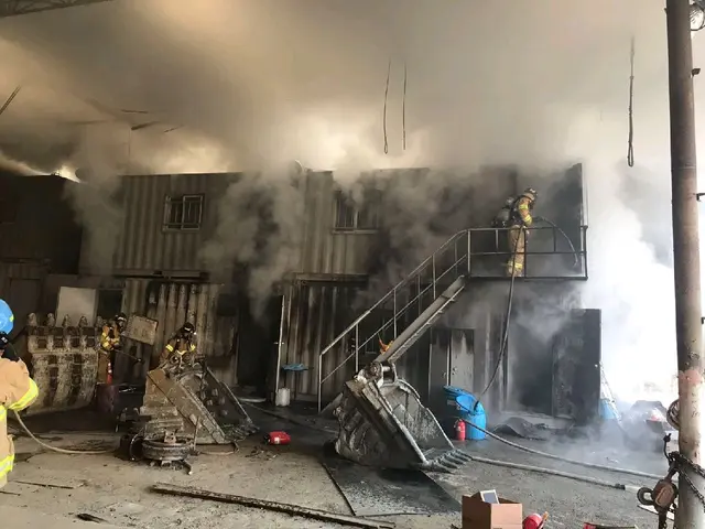 The image shows a group of firefighters working to put out a fire in a warehouse. We can see the...