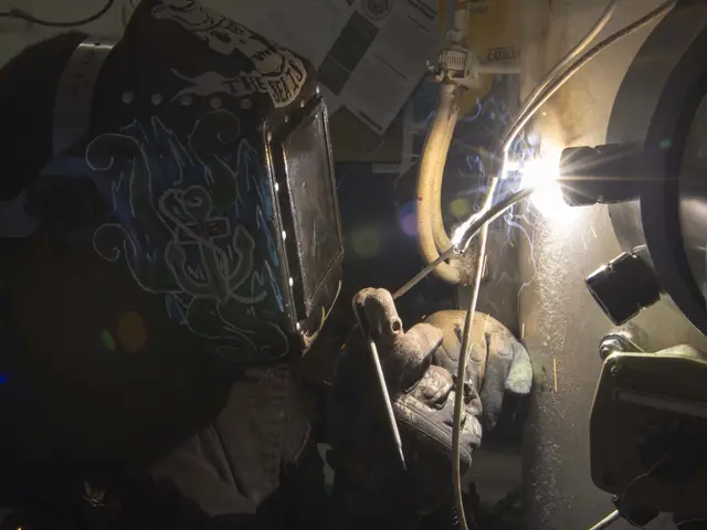 The image shows a welder wearing a helmet and gloves, working on a piece of metal with a welding...