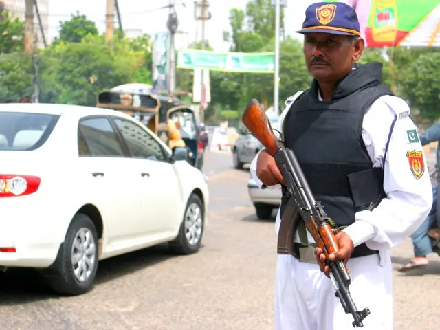 The image shows a police officer standing guard on the side of a road, holding a gun in his hand....