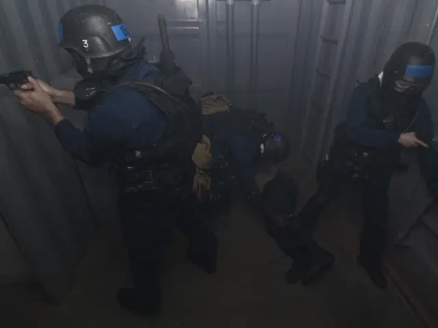 The image shows a group of police officers in riot gear standing next to each other, with one of...