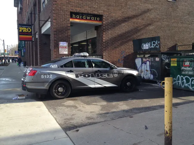 The image shows a police car parked on the side of a street in front of a building with windows and...