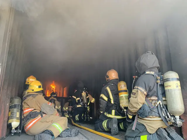 The image shows a group of firefighters wearing helmets and oxygen cylinders, sitting in the back...