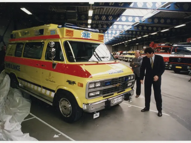The image shows an ambulance parked inside of a building, with a group of people standing on the...
