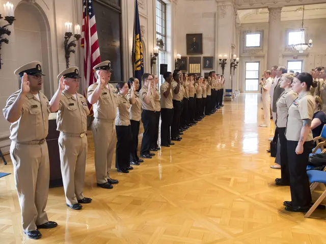 The image shows a group of people in uniform standing in a room with chairs on the right side and a...