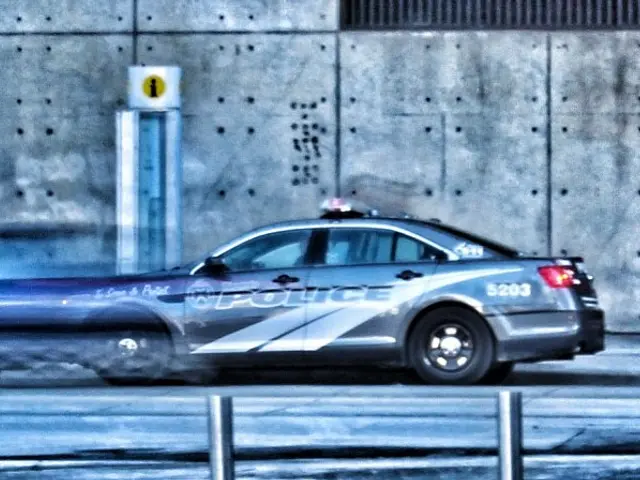 The image shows a police car driving down a street next to a tall building. The car is on the road...