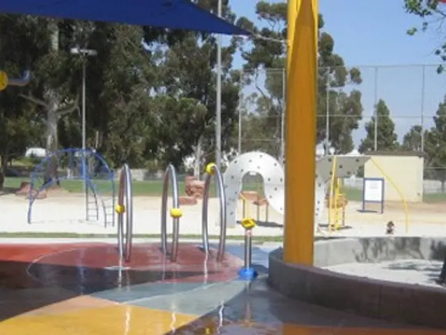 The image shows a playground with a water fountain in the middle of it, surrounded by yellow...