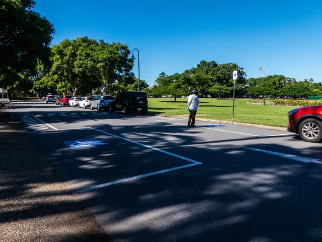 The image shows a man standing in the middle of a parking lot next to a red car. He is wearing a...